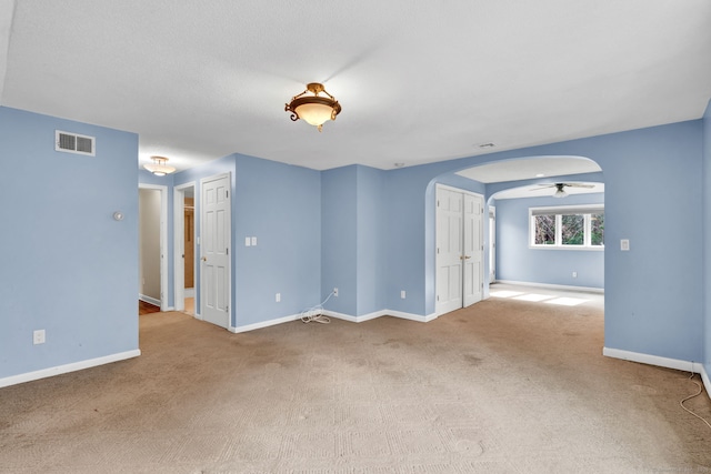 carpeted empty room with arched walkways, baseboards, and ceiling fan