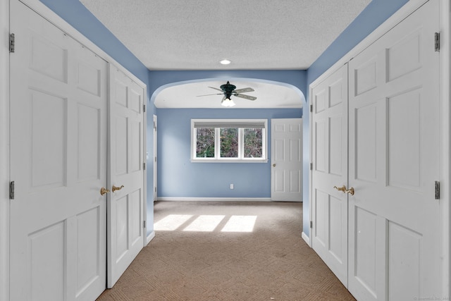 hallway with light carpet, arched walkways, a textured ceiling, baseboards, and recessed lighting