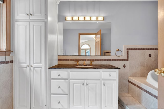 bathroom with tile walls, vanity, and tiled bath