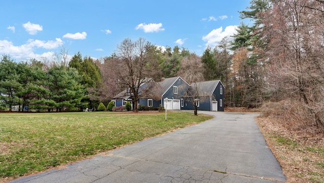 view of front of property featuring a front lawn, a garage, driveway, and view of wooded area