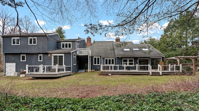 rear view of property with a chimney, a yard, a deck, and roof with shingles
