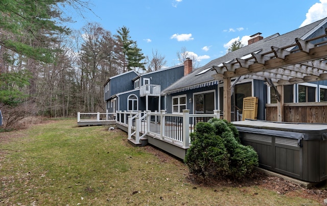 rear view of property featuring a hot tub, a lawn, a wooden deck, a chimney, and a pergola