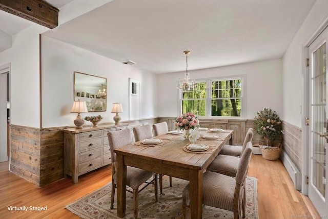 dining space featuring light wood-type flooring, a chandelier, wood walls, and wainscoting