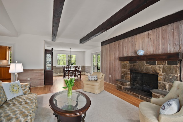 living room featuring a baseboard radiator, wood walls, wood finished floors, a fireplace, and beam ceiling