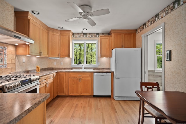 kitchen with a sink, white appliances, wallpapered walls, and a wealth of natural light