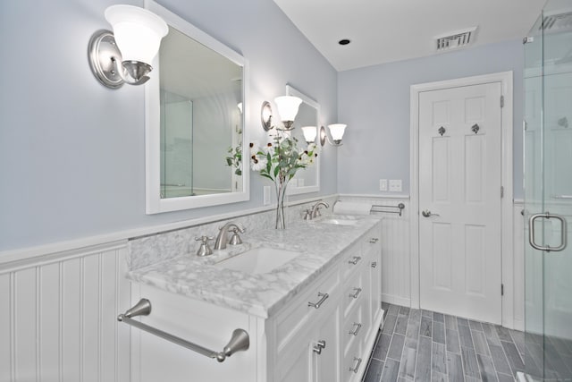 full bathroom featuring double vanity, a sink, visible vents, a shower stall, and wainscoting