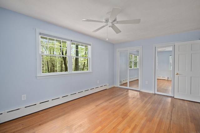 unfurnished bedroom with two closets, light wood-style flooring, and baseboard heating