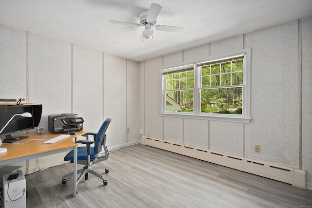 office area featuring a ceiling fan, light wood-type flooring, a decorative wall, and a baseboard radiator