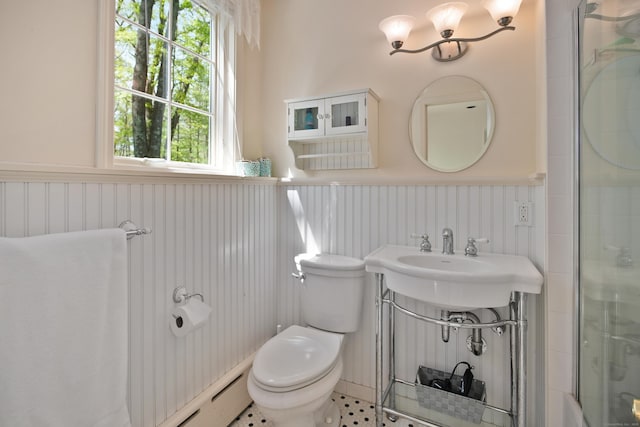 bathroom featuring toilet, a shower with shower door, wainscoting, and a sink