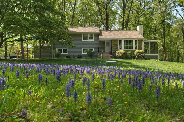 tri-level home with a sunroom, a chimney, and a front yard