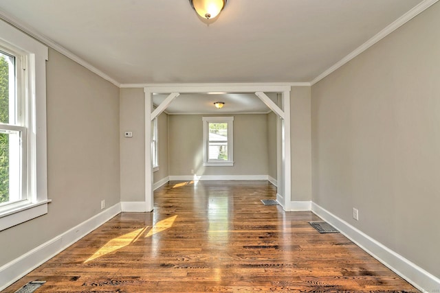empty room with crown molding, baseboards, dark wood-style floors, and visible vents