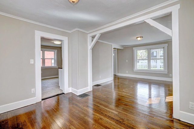 empty room featuring baseboards, ornamental molding, visible vents, and wood finished floors