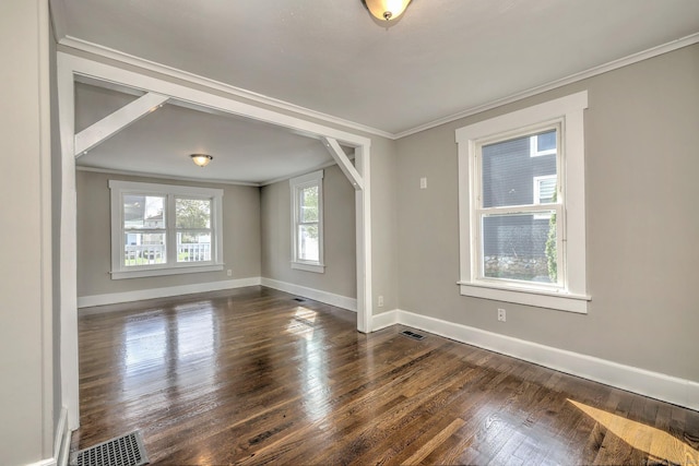 spare room featuring dark wood-style flooring, crown molding, visible vents, and baseboards