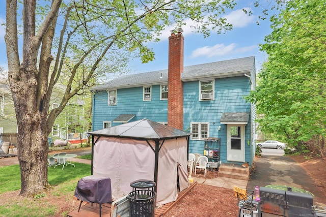rear view of house featuring a shingled roof, a chimney, entry steps, and a gazebo