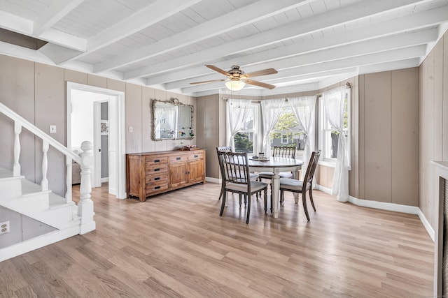 dining room featuring light wood-style flooring, a ceiling fan, stairway, beamed ceiling, and baseboards