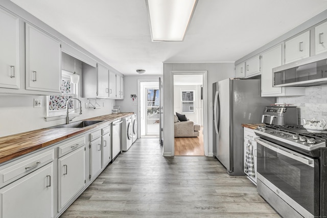 kitchen featuring stainless steel appliances, a sink, light wood-type flooring, wood counters, and backsplash