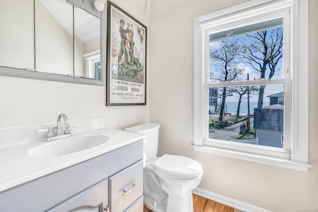 half bathroom with baseboards, toilet, vanity, and wood finished floors
