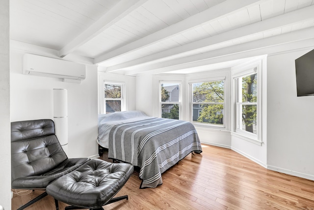 bedroom with an AC wall unit, beam ceiling, light wood finished floors, and baseboards
