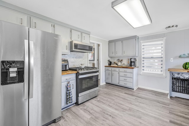 kitchen featuring appliances with stainless steel finishes, wooden counters, light wood-style flooring, ornamental molding, and backsplash
