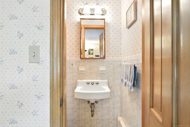 bathroom with wallpapered walls, a sink, a wainscoted wall, and tile walls