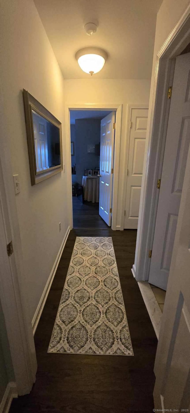 corridor featuring baseboards and dark wood finished floors