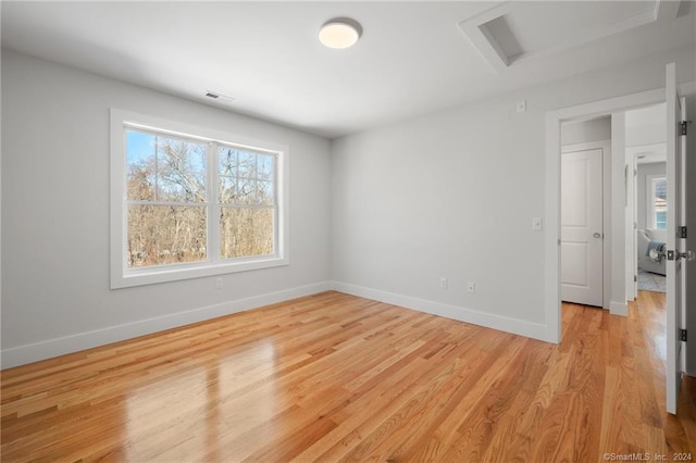 empty room with light wood-type flooring, baseboards, and attic access
