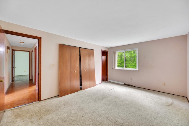 unfurnished bedroom featuring a closet, attic access, visible vents, carpet flooring, and baseboards