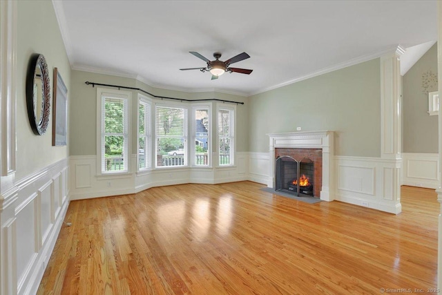 unfurnished living room with light wood finished floors, ceiling fan, a brick fireplace, a decorative wall, and a wainscoted wall