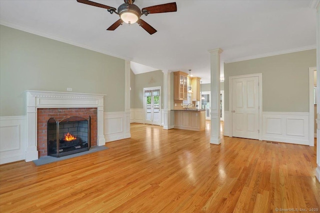 unfurnished living room with a decorative wall, a wainscoted wall, light wood finished floors, a brick fireplace, and a ceiling fan