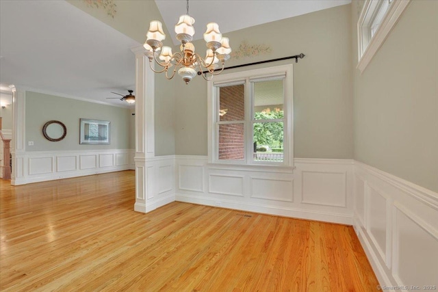 unfurnished dining area with ceiling fan with notable chandelier, a wainscoted wall, and plenty of natural light