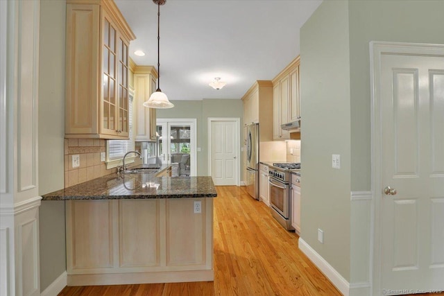 kitchen featuring glass insert cabinets, a sink, dark stone counters, tasteful backsplash, and appliances with stainless steel finishes