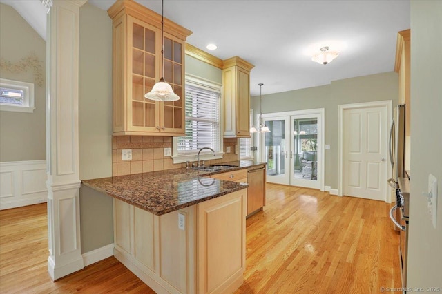 kitchen with a peninsula, light wood finished floors, glass insert cabinets, a sink, and dark stone counters