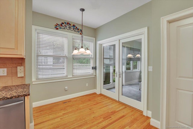 unfurnished dining area featuring baseboards, light wood finished floors, french doors, and a chandelier
