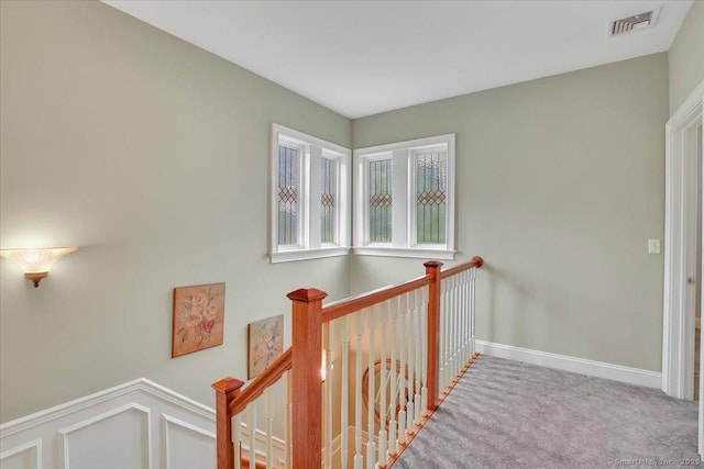 hallway with an upstairs landing, carpet, baseboards, and visible vents