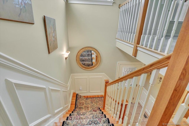 staircase with a decorative wall, wainscoting, and a towering ceiling