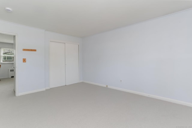 unfurnished bedroom with light colored carpet, radiator heating unit, and baseboards