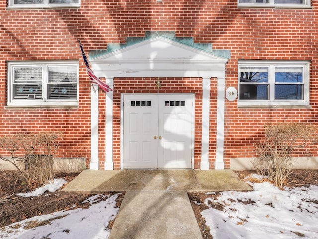 snow covered property entrance featuring brick siding