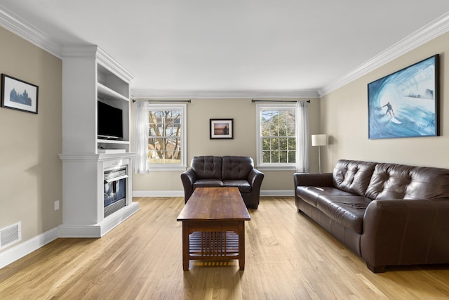 living area with baseboards, ornamental molding, a glass covered fireplace, and light wood-style floors