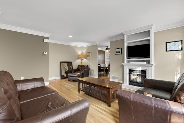living area with visible vents, light wood-style flooring, a ceiling fan, and ornamental molding