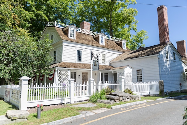 second empire-style home featuring a fenced front yard and a chimney