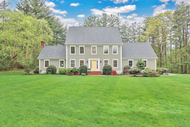 colonial home featuring a chimney, a front yard, and roof with shingles