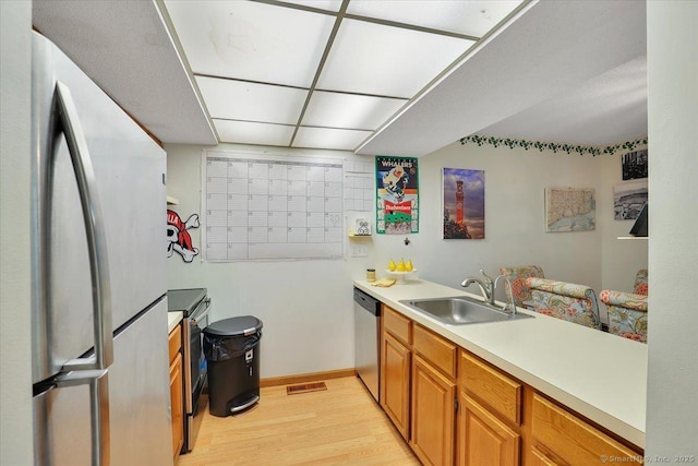 kitchen featuring appliances with stainless steel finishes, a sink, light wood-type flooring, light countertops, and baseboards