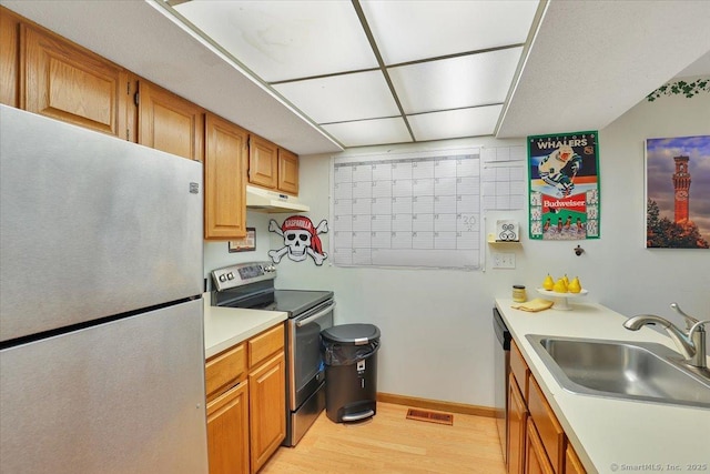 kitchen with stainless steel appliances, a sink, under cabinet range hood, light wood-type flooring, and light countertops
