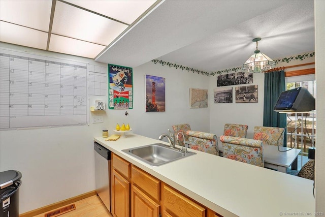 kitchen featuring a sink, a peninsula, stainless steel dishwasher, light countertops, and baseboards