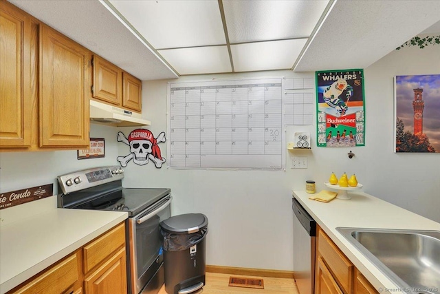 kitchen featuring stainless steel appliances, under cabinet range hood, light countertops, a sink, and baseboards