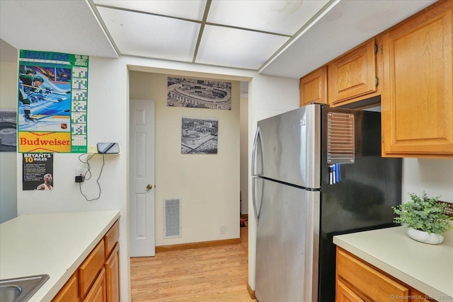 kitchen featuring freestanding refrigerator, light wood finished floors, light countertops, and brown cabinetry