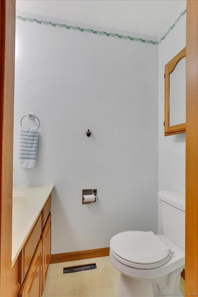 bathroom with a textured ceiling, toilet, vanity, tile patterned floors, and baseboards