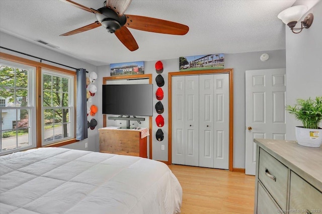 bedroom featuring a textured ceiling, light wood-style flooring, a closet, and ceiling fan
