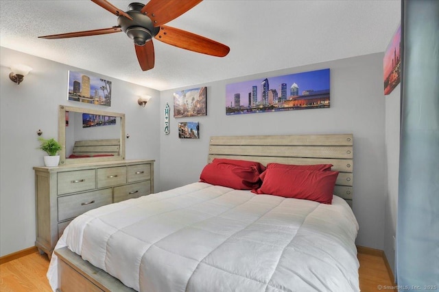 bedroom with light wood finished floors, baseboards, a ceiling fan, and a textured ceiling