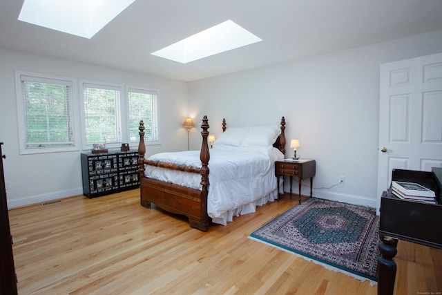 bedroom featuring baseboards, wood finished floors, a skylight, and visible vents